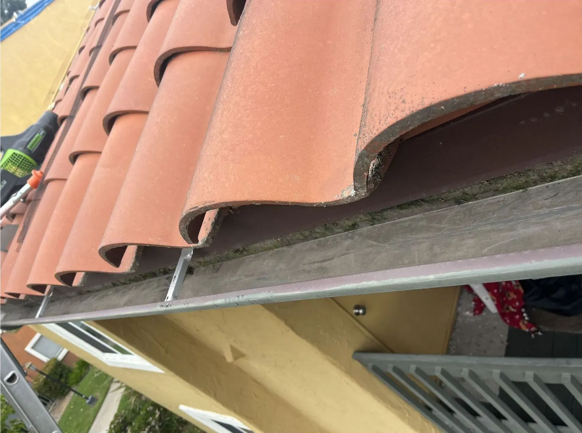 Close-up of terracotta roof tiles at a roof edge with gutter and building siding below