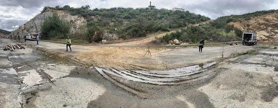 Collapsed road in a rocky hillside area with people standing nearby and a truck on the right.