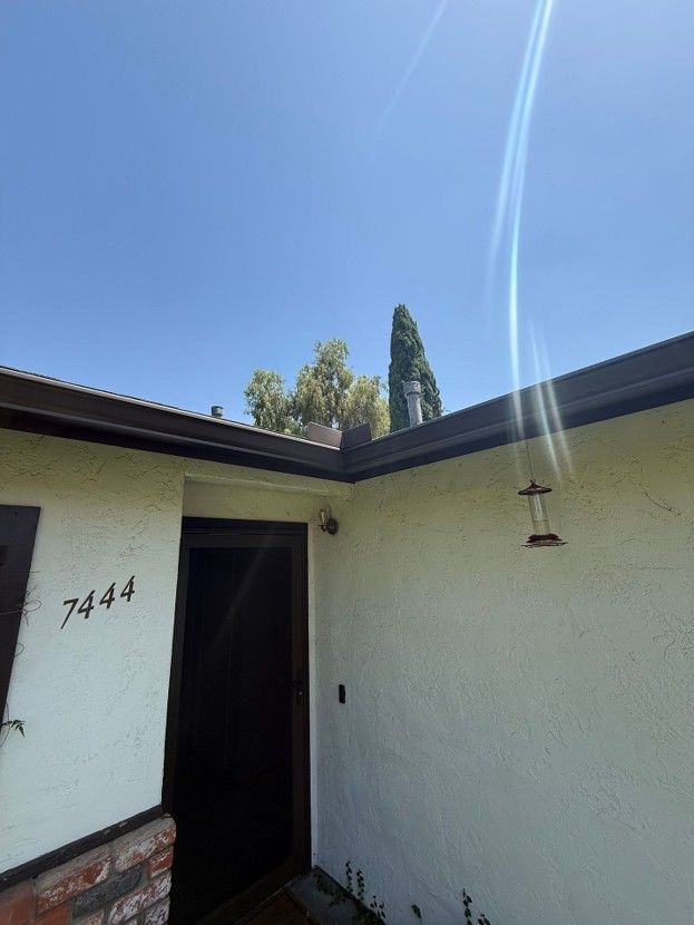Front entry of a white stucco house with the number 7444, open doorway, and bright blue sky.