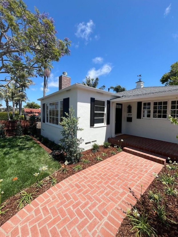 White house with brick walkway, front porch, and green yard under a blue sky