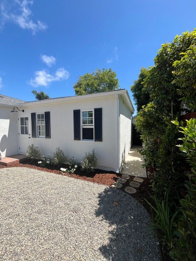White house exterior with dark shutters, gravel driveway, and blue sky