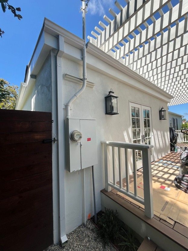 White exterior side entrance with a wooden gate, lantern light, and small porch railing under a blue sky.