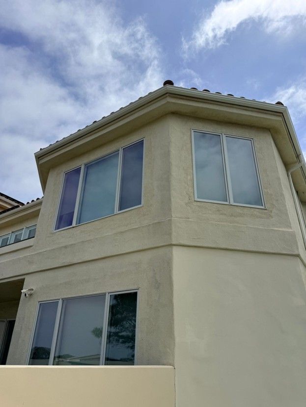 Beige two-story house corner with large windows under a cloudy sky