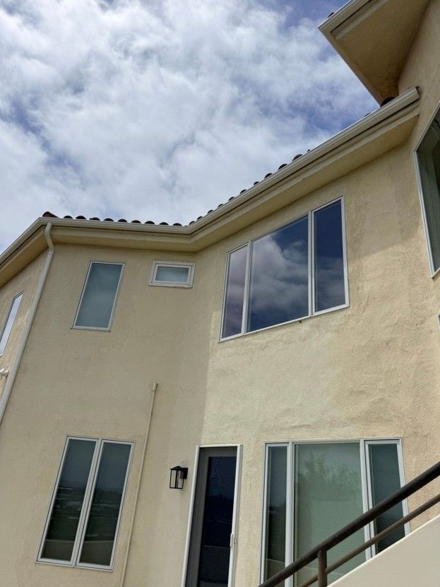 Two-story beige stucco house with large windows and a cloudy sky above