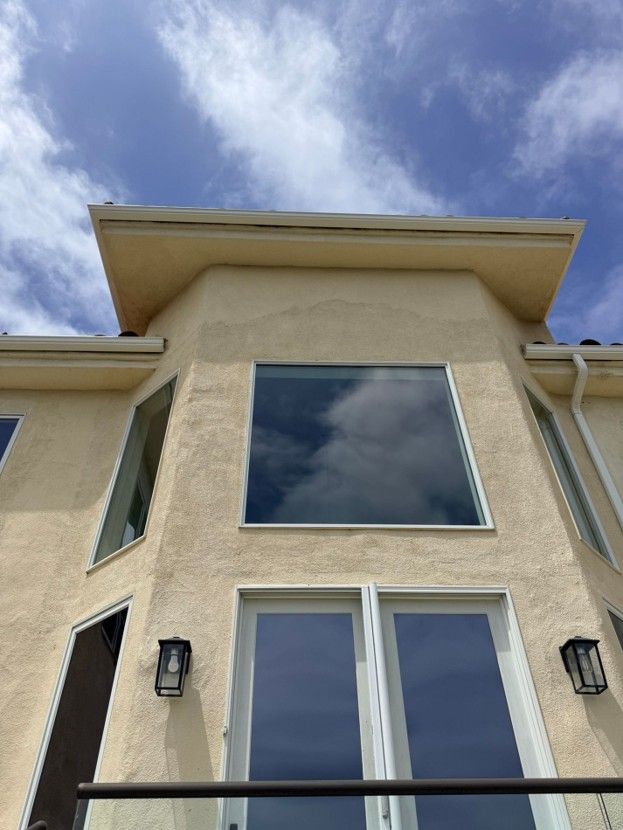 Low-angle view of a beige stucco house facade with large windows against a blue sky