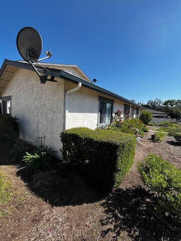 Suburban house with satellite dish, trimmed hedges, and a sunny blue sky