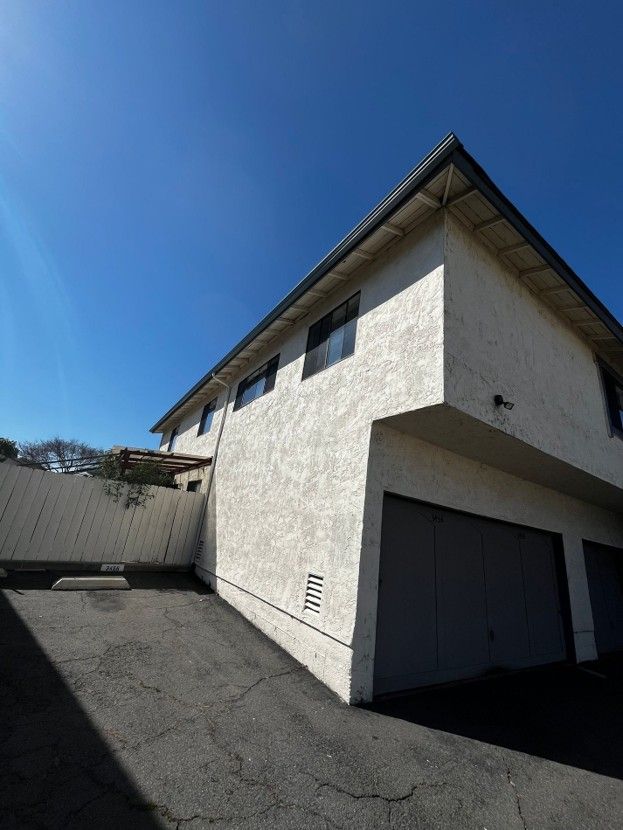 White two-story house with dark garage doors and sloped driveway under a clear blue sky