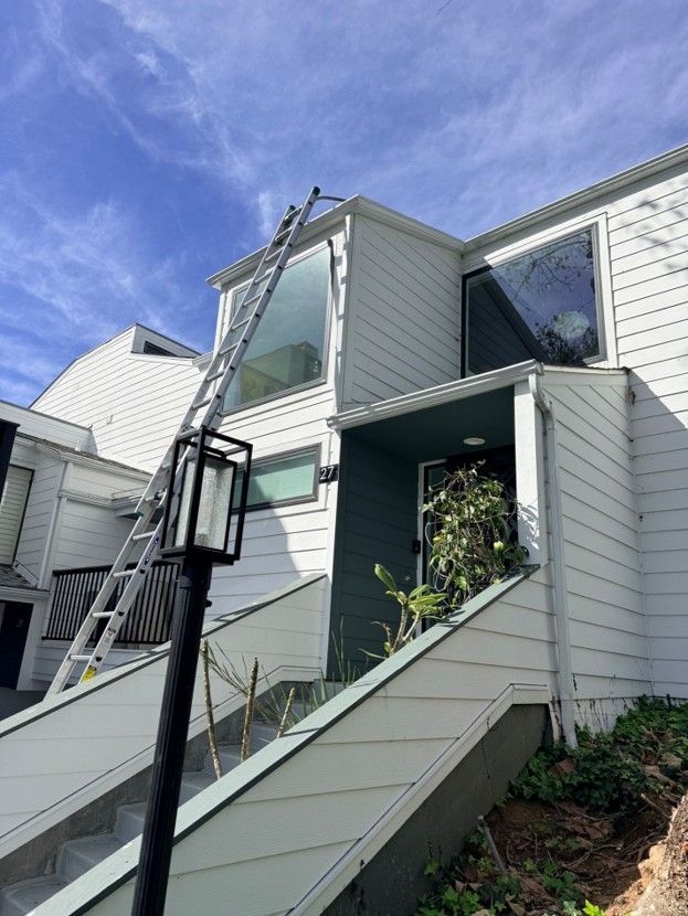 Exterior of a townhouse with a window-cleaning ladder and a person working near the upper windows