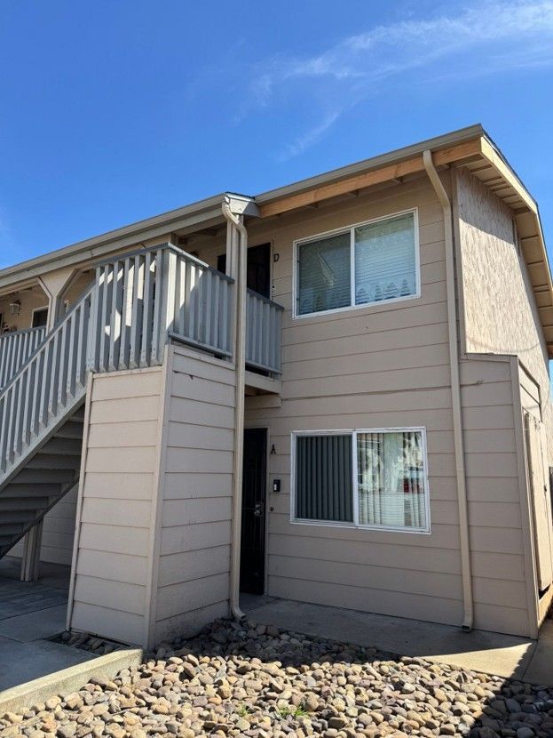 Apartment exterior with beige siding, white railings, windows, and an exterior staircase under a blue sky