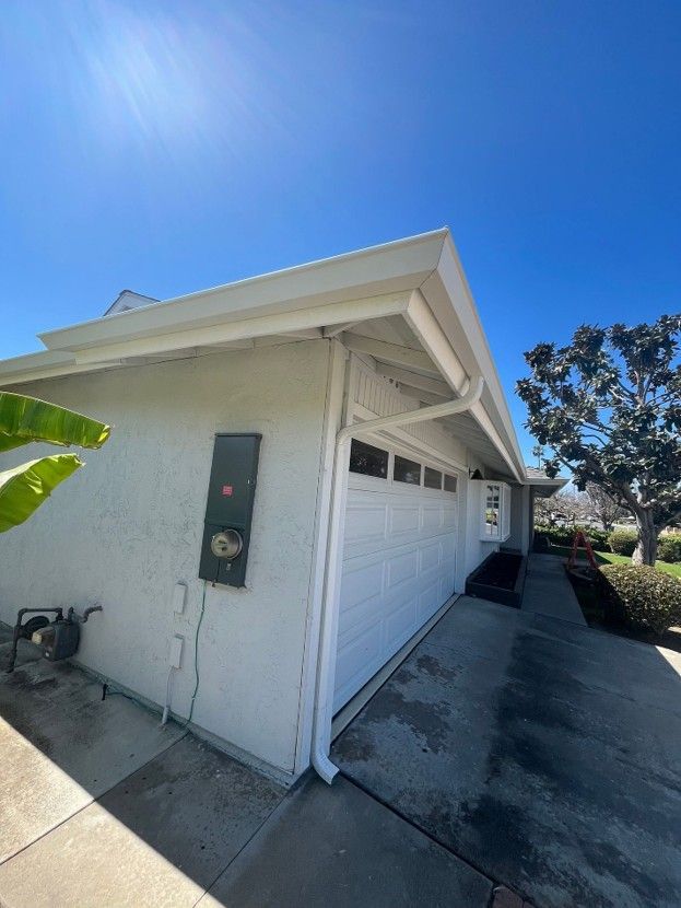 White house exterior with garage door, side entry, and concrete driveway under a bright blue sky