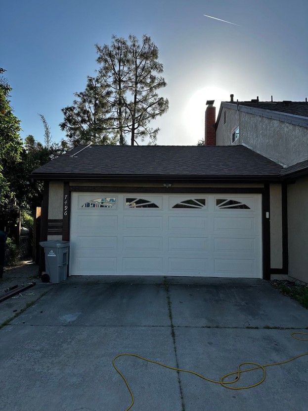 Single-story garage with white door and dark trim, seen from a driveway under a clear blue sky.