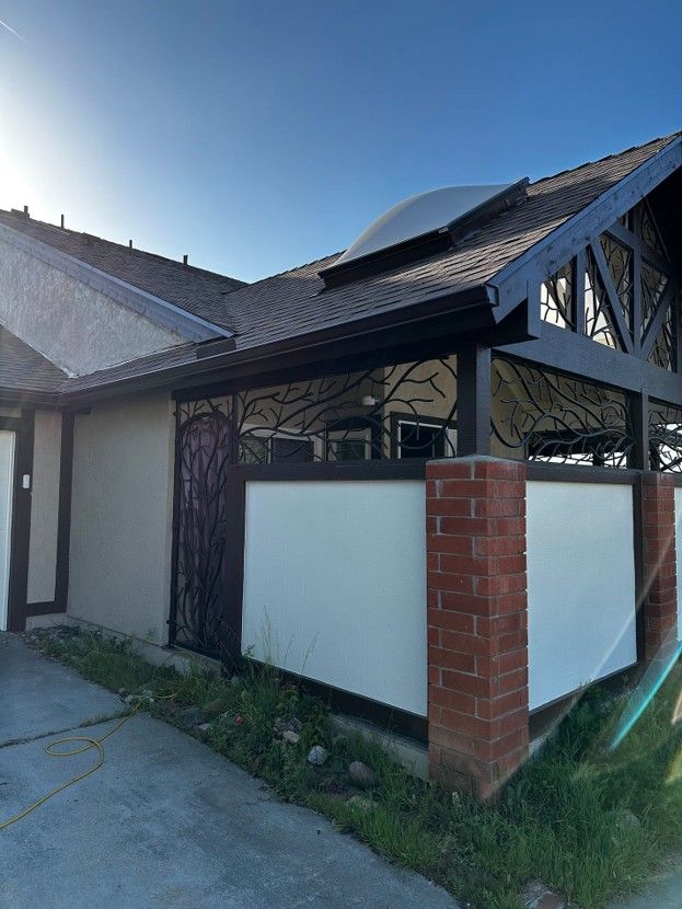 Exterior of a house with a dark tiled roof, white walls, brick pillar, and decorative black trim in sunlight