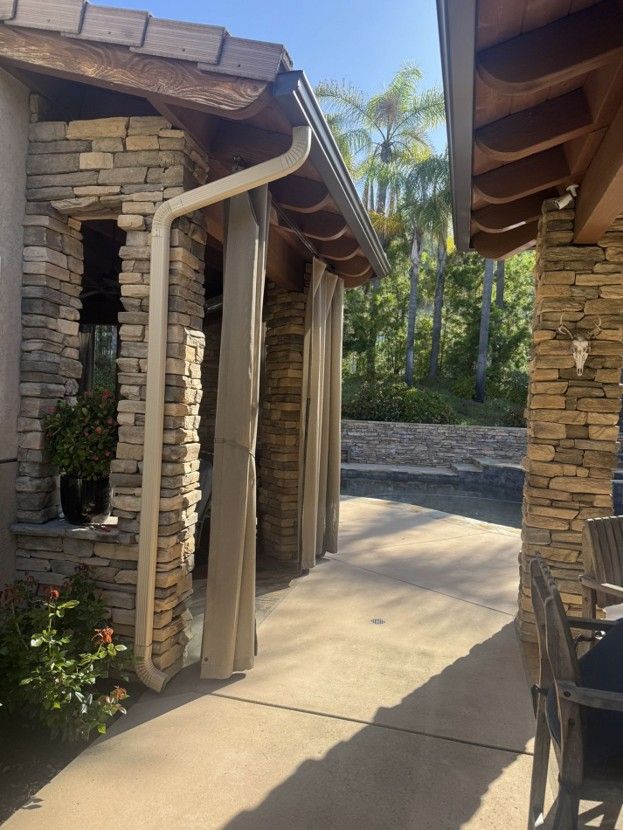 Stone building corridor with beige curtains, concrete walkway, and palm trees in bright sunlight