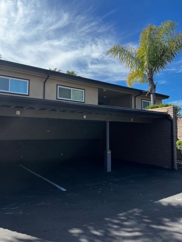 Two-story house with a dark carport and a palm tree against a blue sky