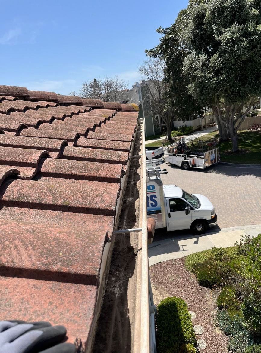 Roof edge overlooking a parking lot with white vans, trees, and a blue sky