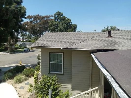 Residential roof and side wall with a window, viewed from above near a street and trees