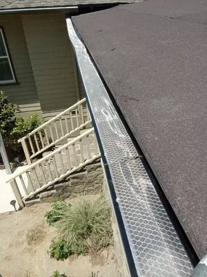 Steep roof with metal gutter guard beside a house and porch railing