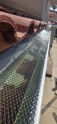 Close-up of a metal mesh gutter guard catching leaves under a brown shingle roof edge