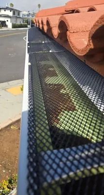 Black mesh gutter guard under orange roof tiles along a rooftop edge