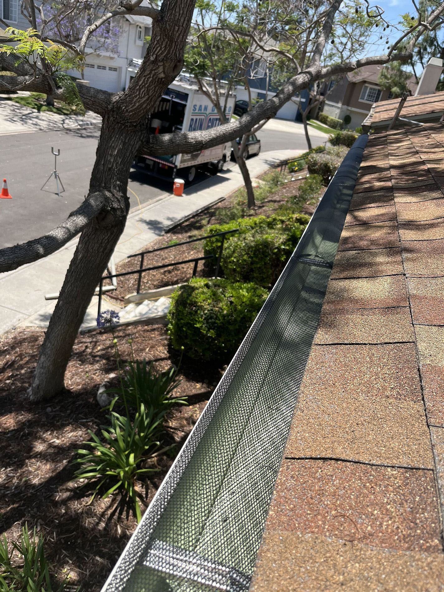 Residential rooftop with tree branches, street below, and orange traffic cones near a sidewalk