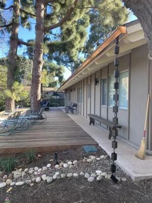 Wooden deck beside a gray house with a porch swing and tall pine trees