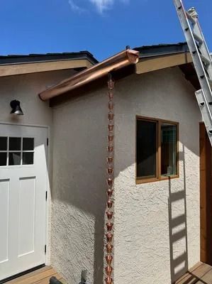 Exterior corner of a stucco house with a white door, brown trim, window, and a ladder leaning against the wall.