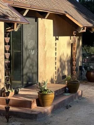 Small front porch with steps, potted plants, and a glass door on a tan house