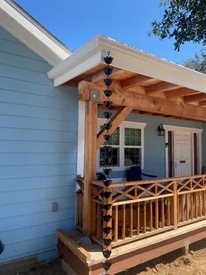 Small covered porch with wood railing, blue siding, and hanging heart-shaped decoration beside white doors.