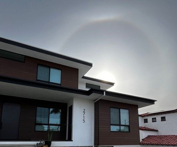 Modern two-story house with dark siding and a faint rainbow in the cloudy sky