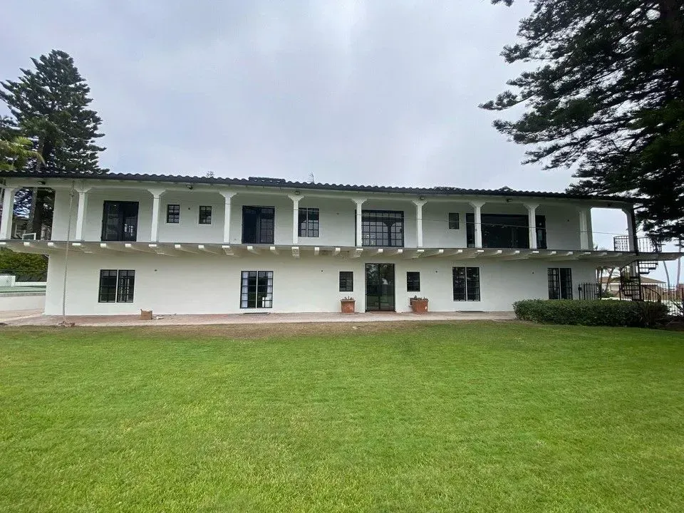 Two-story white house with a long porch, green lawn, and tall trees on either side