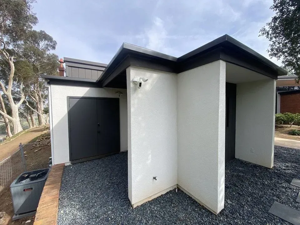 Modern white exterior with dark roof and gravel ground, showing a side entrance and open utility area
