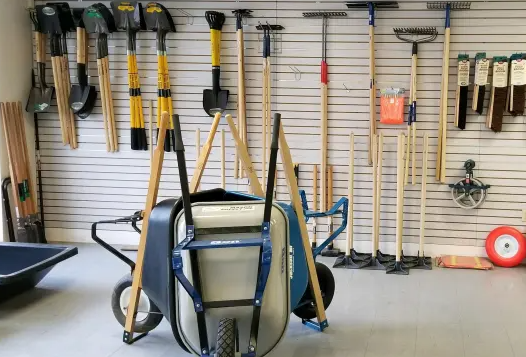 A wheelbarrow is sitting in front of a wall full of gardening tools.
