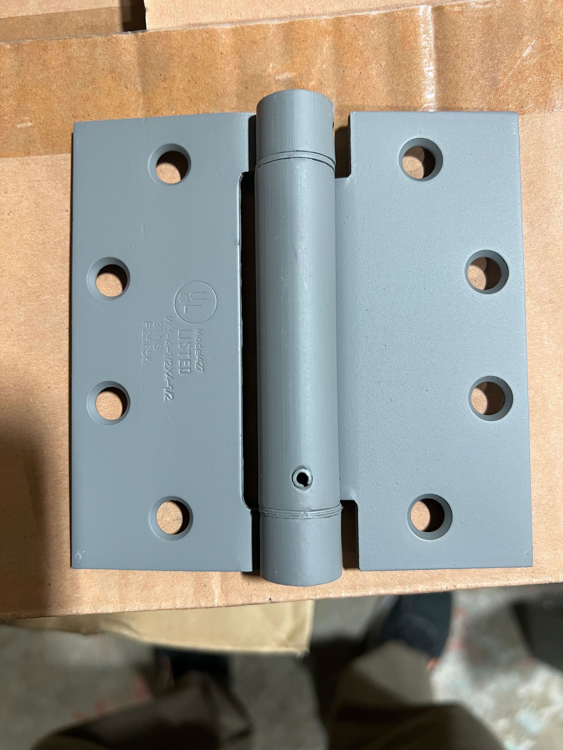 A gray door hinge is sitting on top of a cardboard box