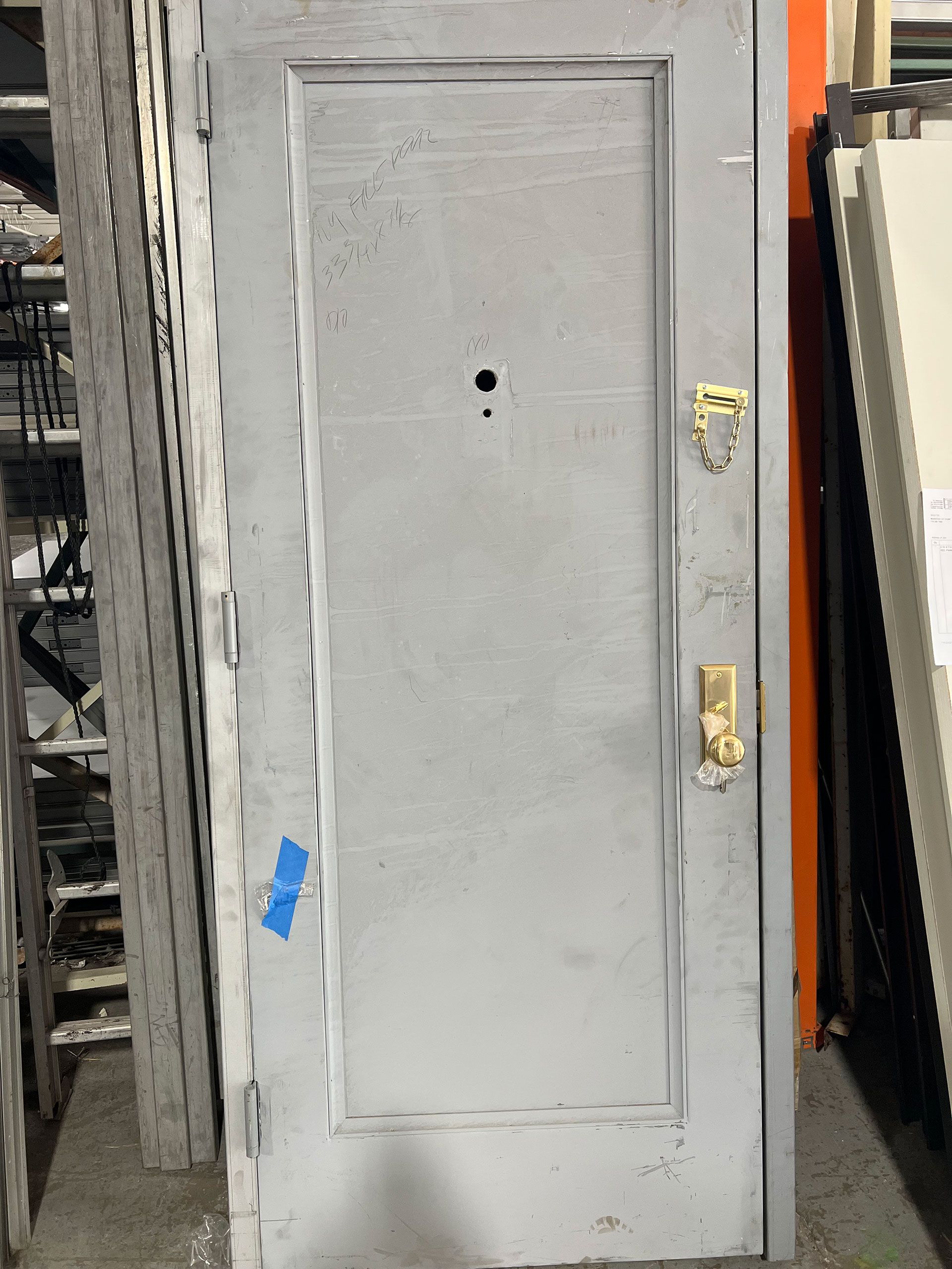 A white door with a gold handle is sitting in a warehouse