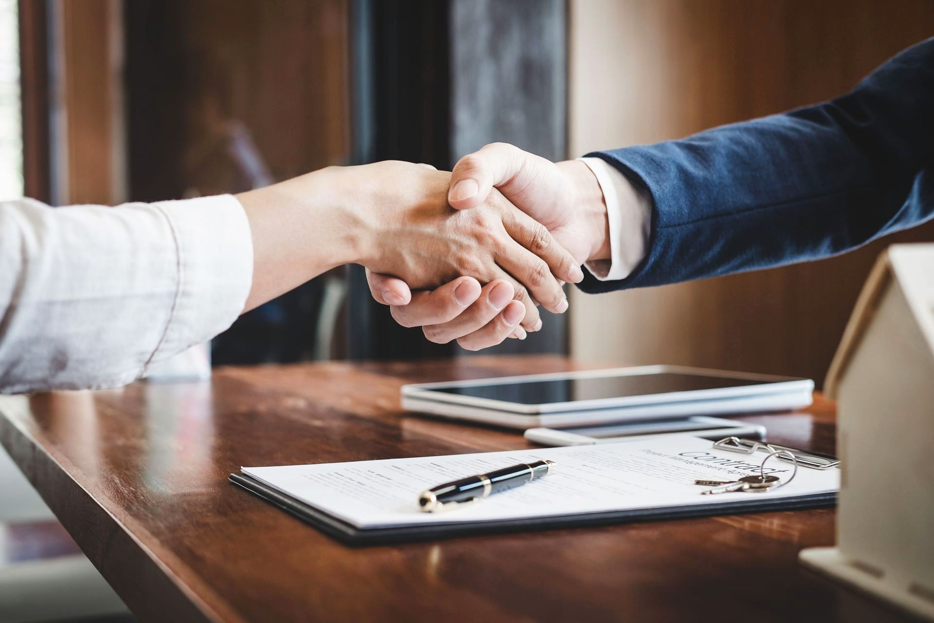 Two people shaking hands over a contract and keys on a wooden table.