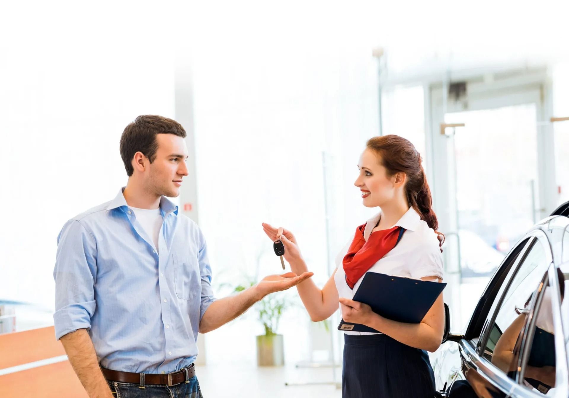A car salesperson handing car keys to a customer in a showroom.