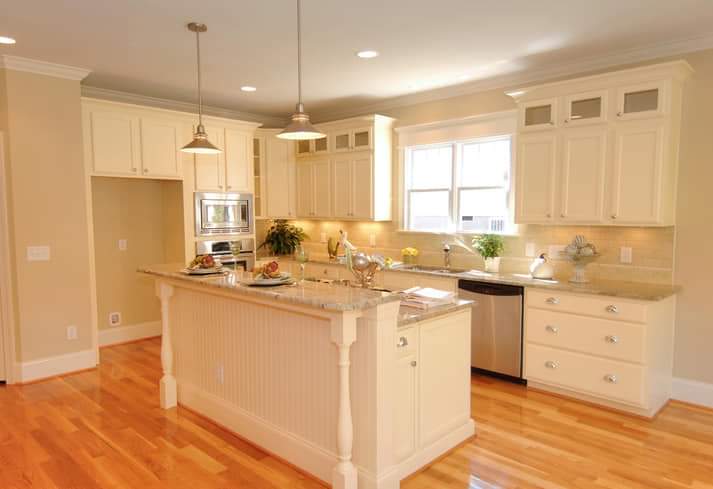 A kitchen with white cabinets , granite counter tops , stainless steel appliances and hardwood floors.