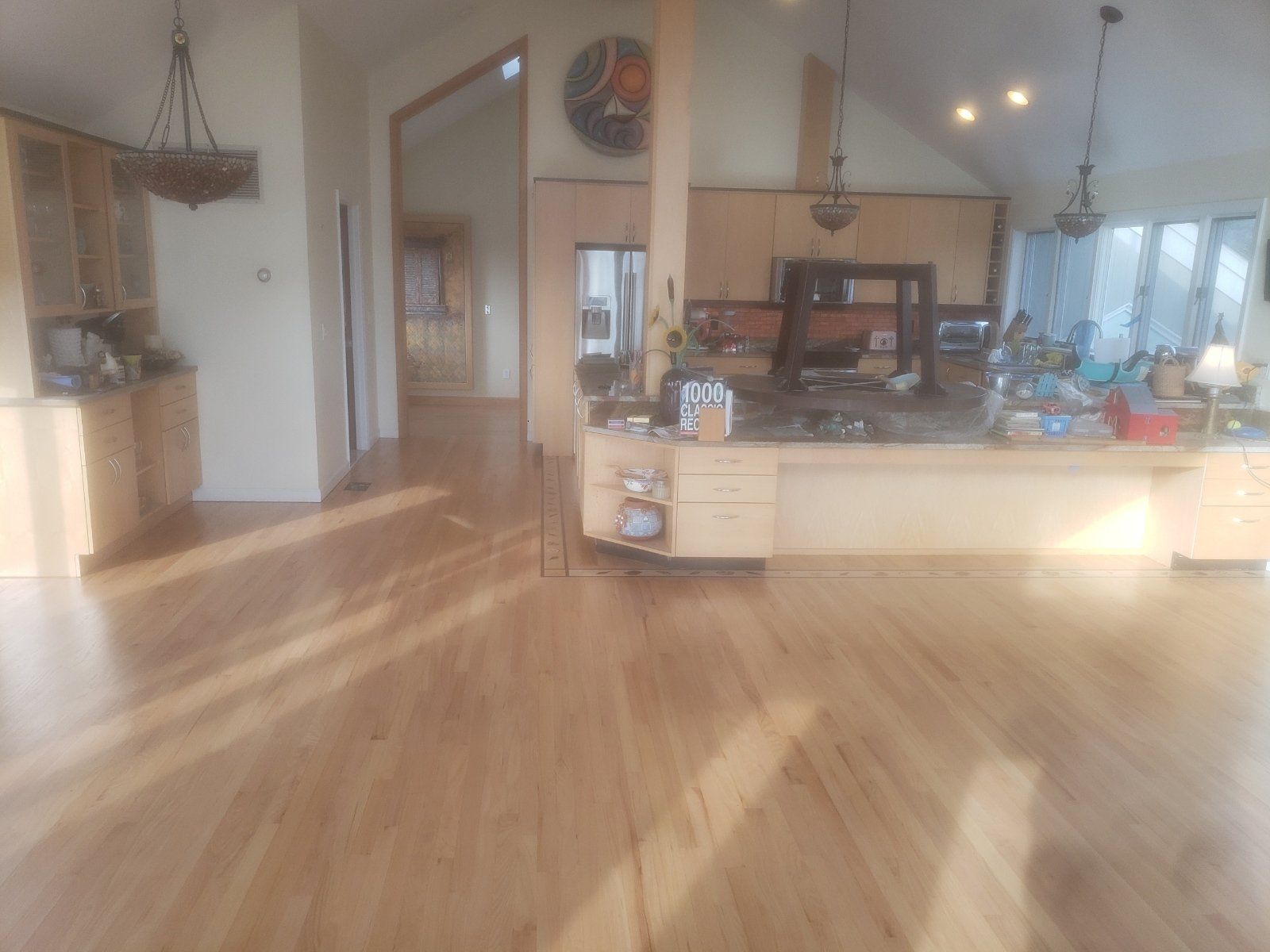 A large room with a wooden floor and a kitchen in the background.