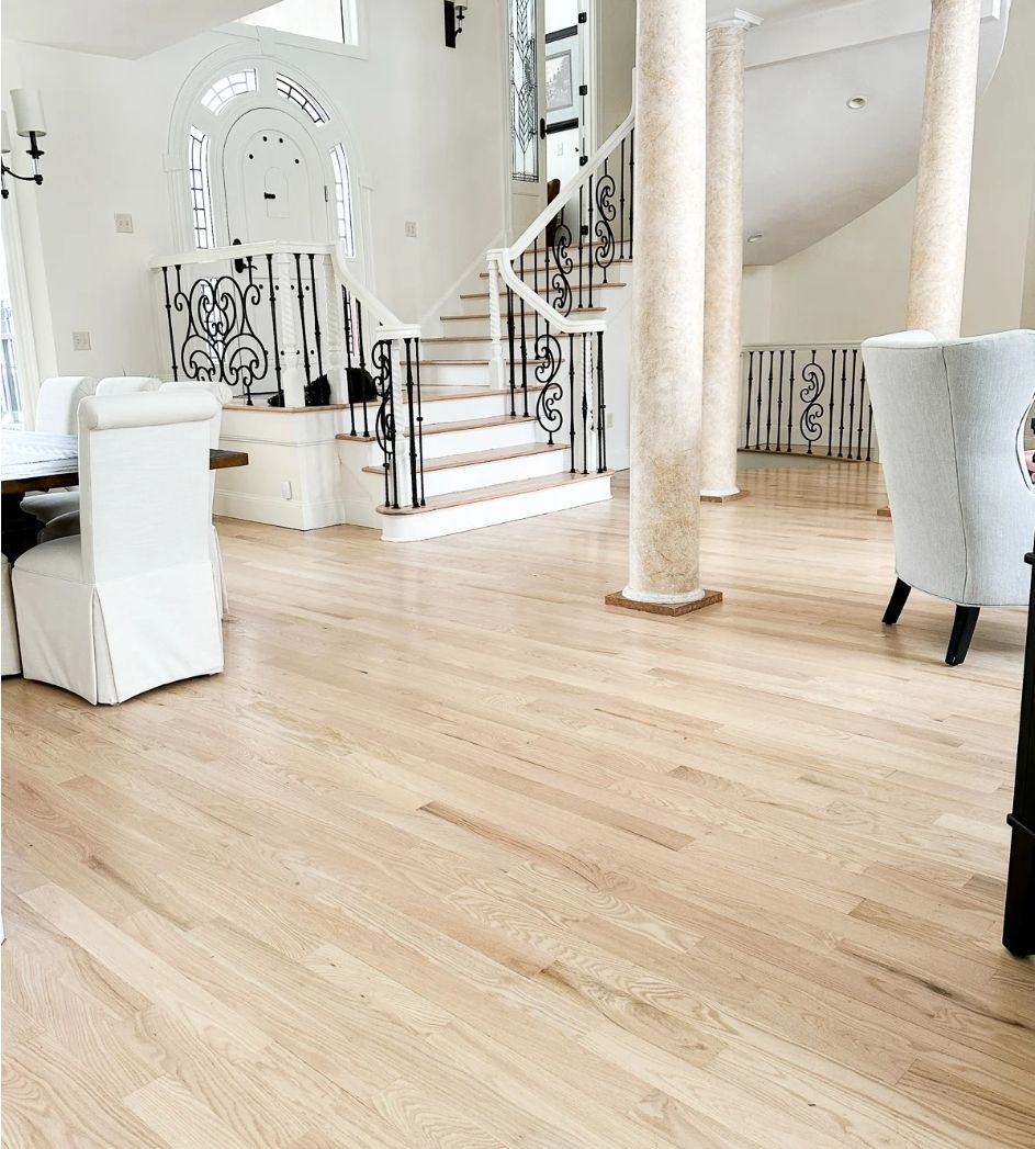 A living room with hardwood floors and white chairs and stairs.
