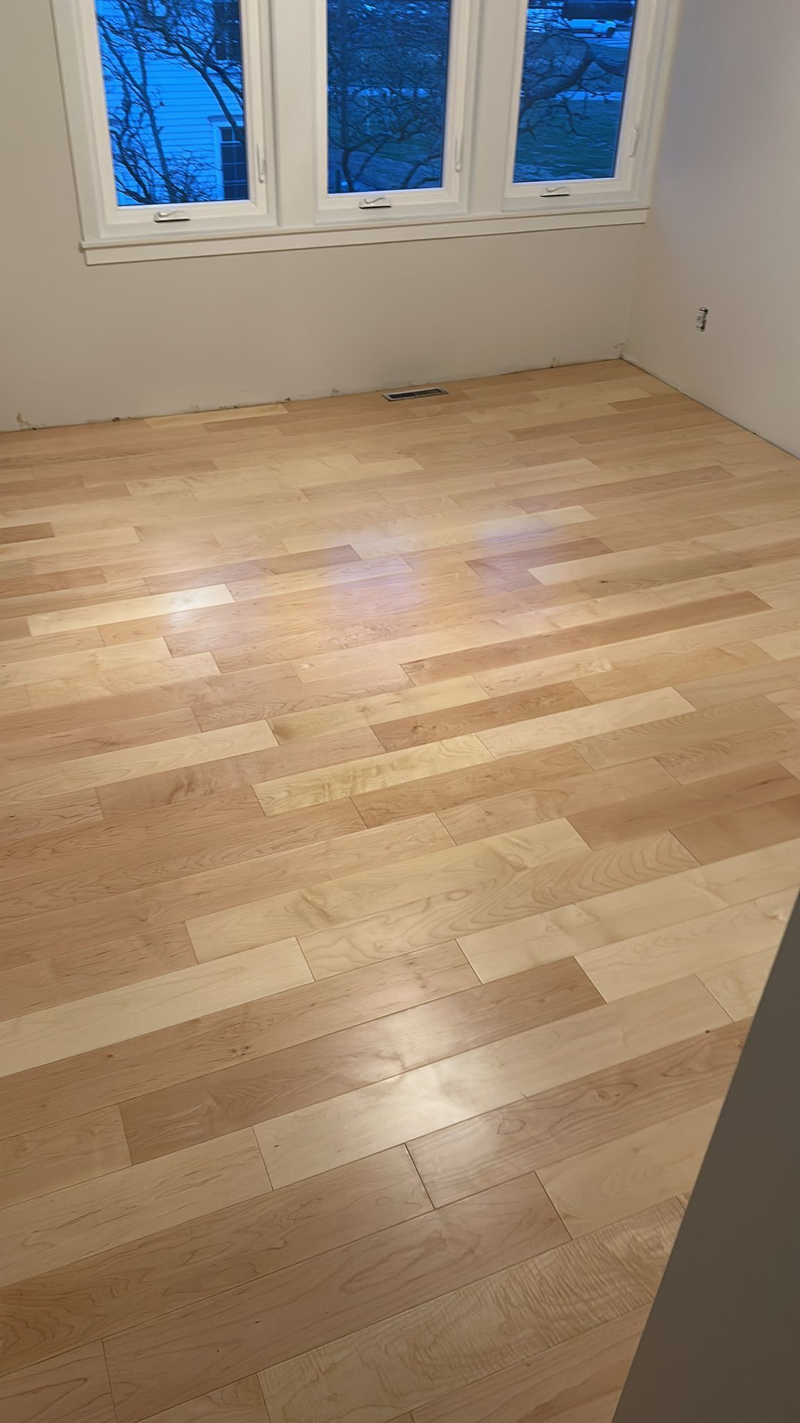 A room with a wooden floor and three windows.