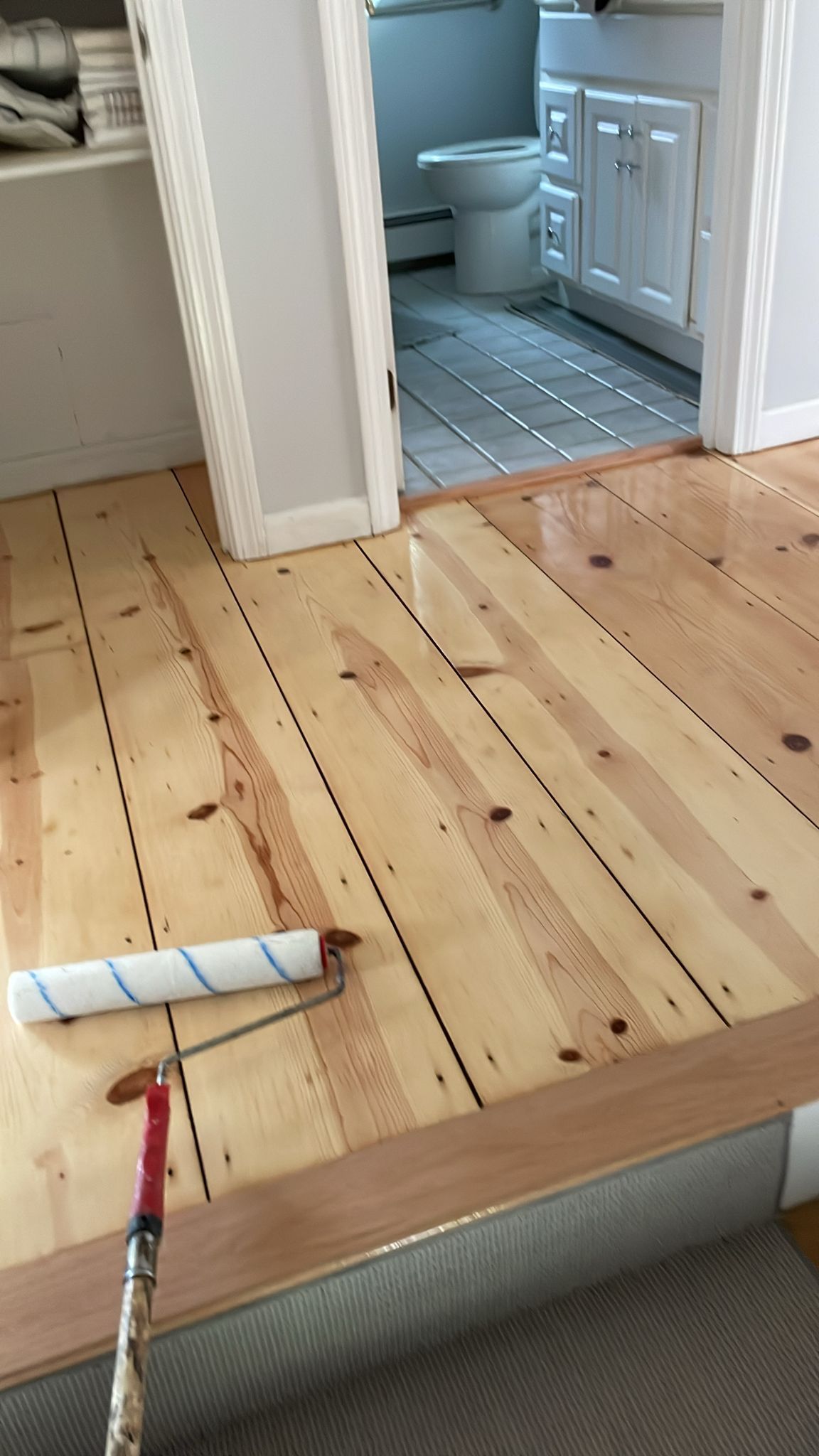 A roller is being used to paint a wooden floor in a bathroom.