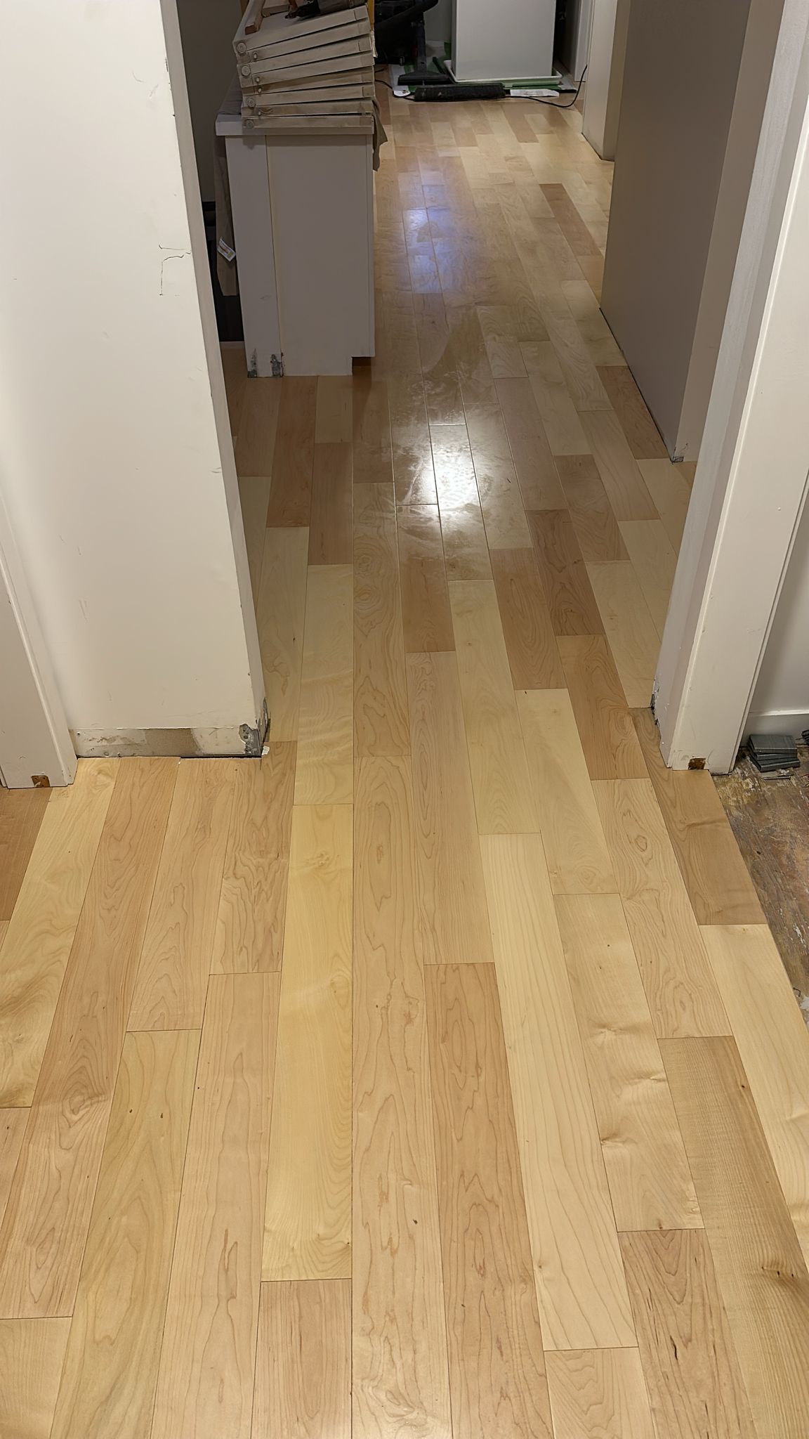 A wooden floor in a hallway leading to a kitchen.