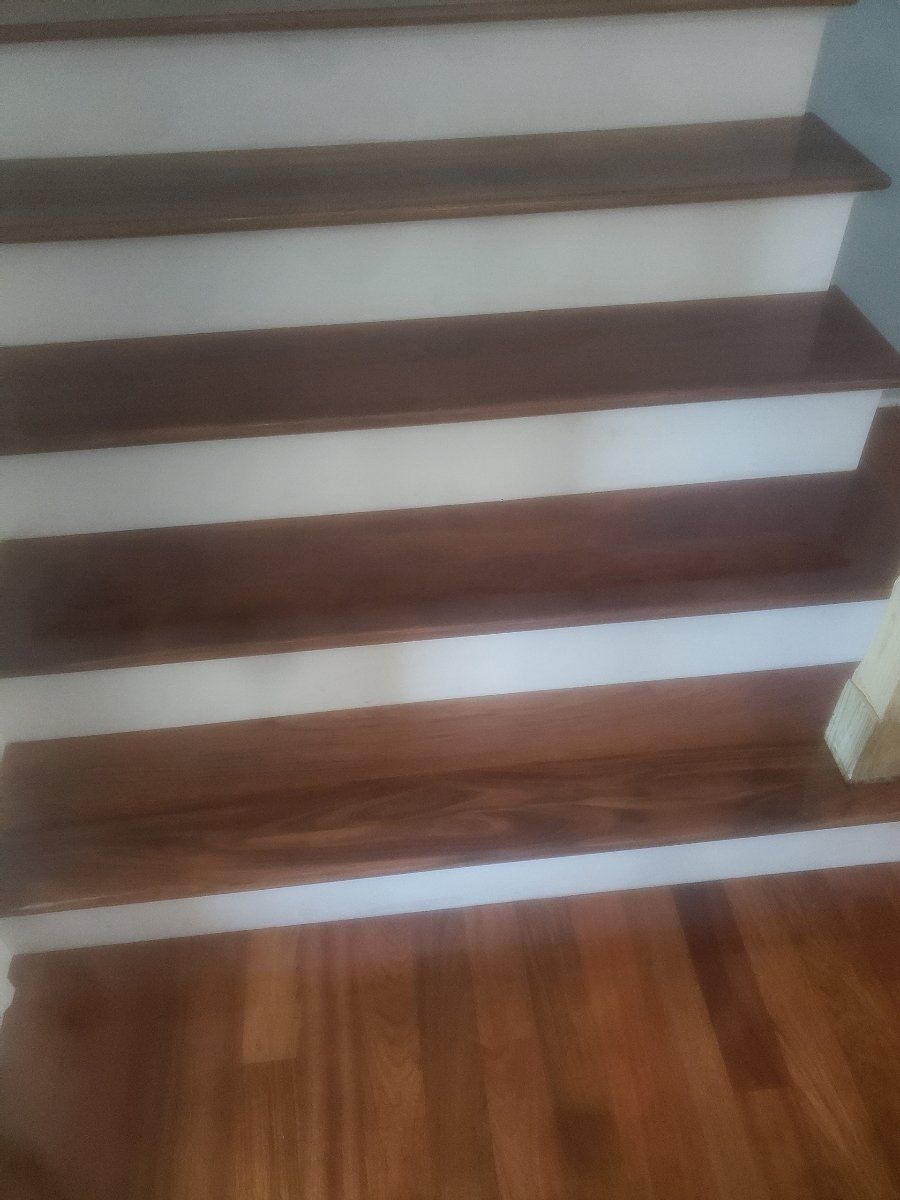 A close up of a wooden staircase with white steps and a wooden floor.