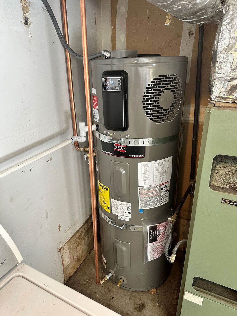A tall, gray water heater with copper pipes installed in a utility room, next to a green appliance.
