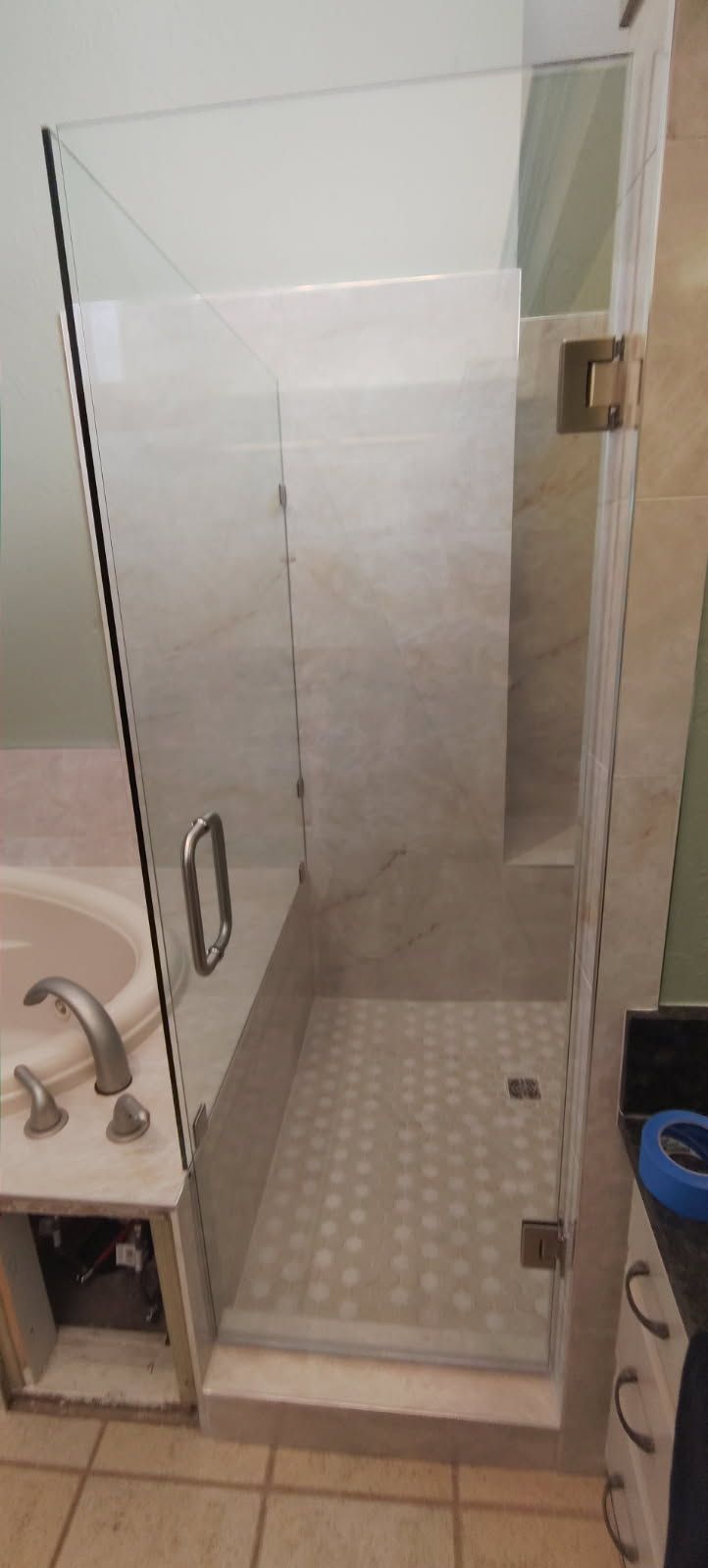 Small tiled shower stall with a glass door and chrome handle in a bathroom.