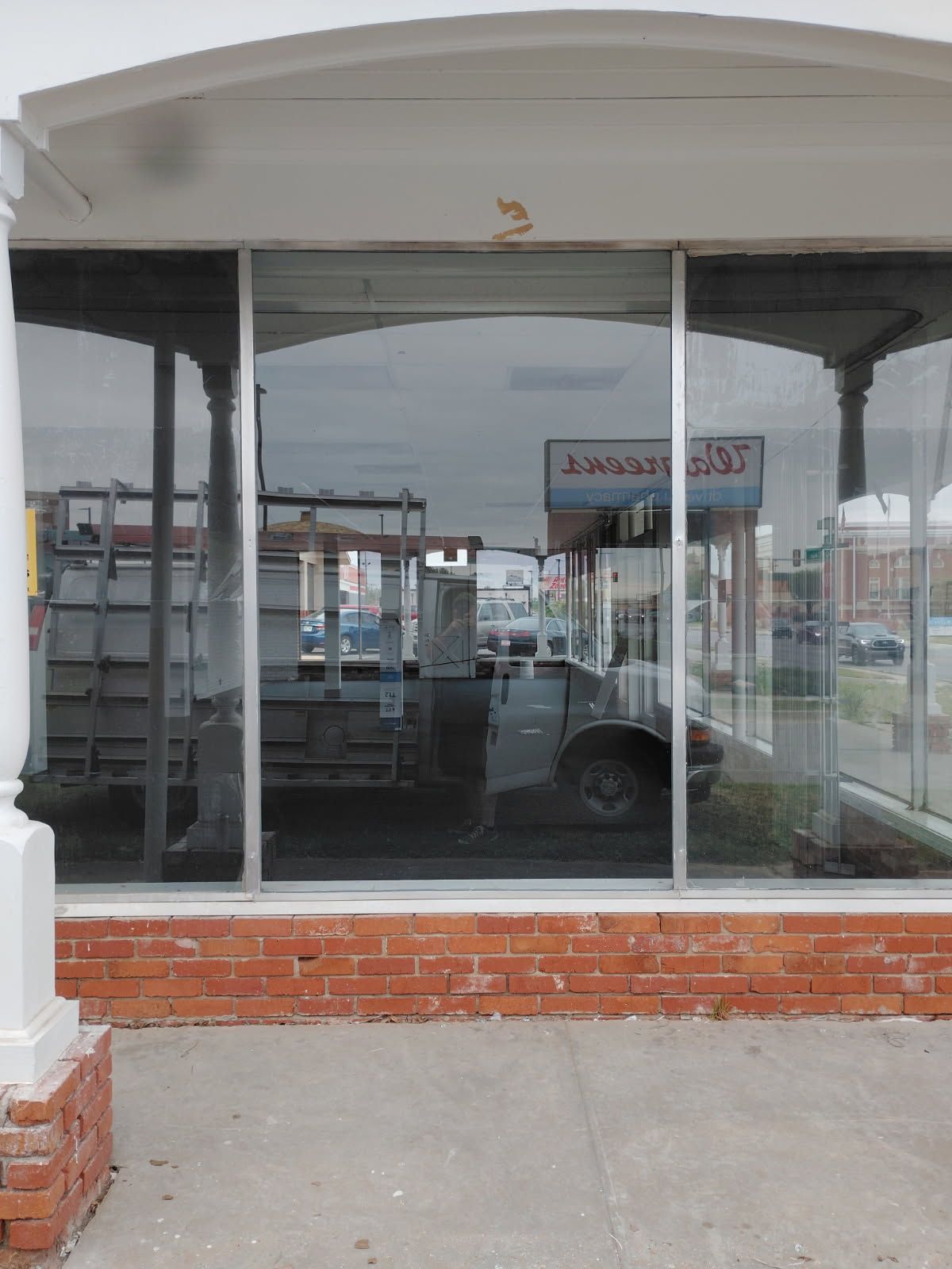 Empty storefront with large glass windows, brick base, and a concrete sidewalk in front