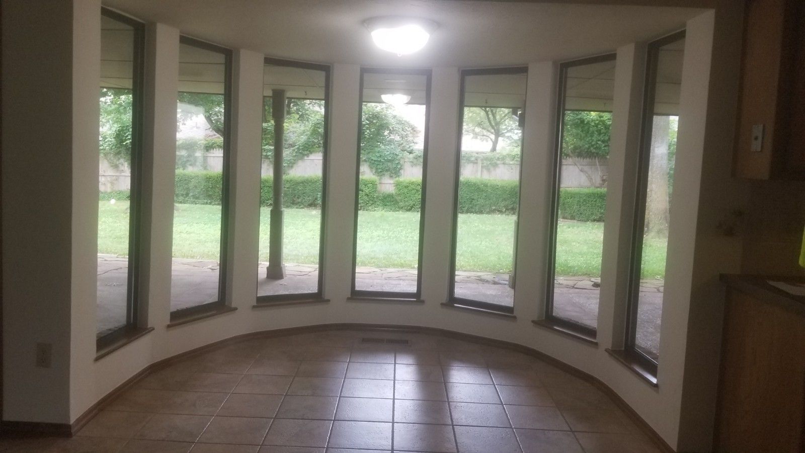 Curved sunroom with floor-to-ceiling windows, tiled floor, and view of a green backyard.