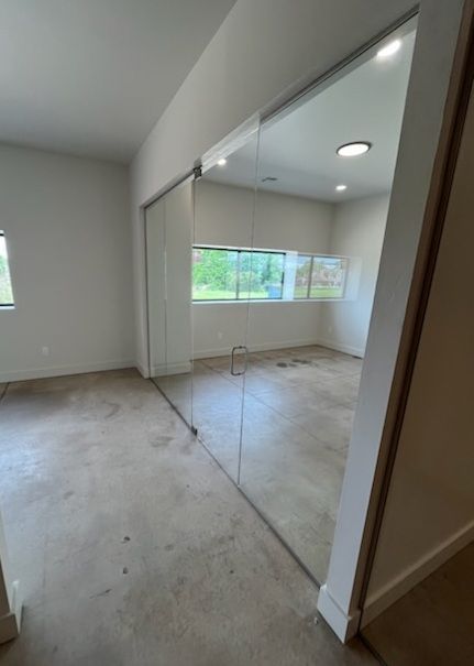Small empty room with mirrored closet doors, window light, and bare concrete floor