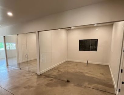 Empty modern room with glass wall and beige concrete floor, lit by recessed ceiling lights.