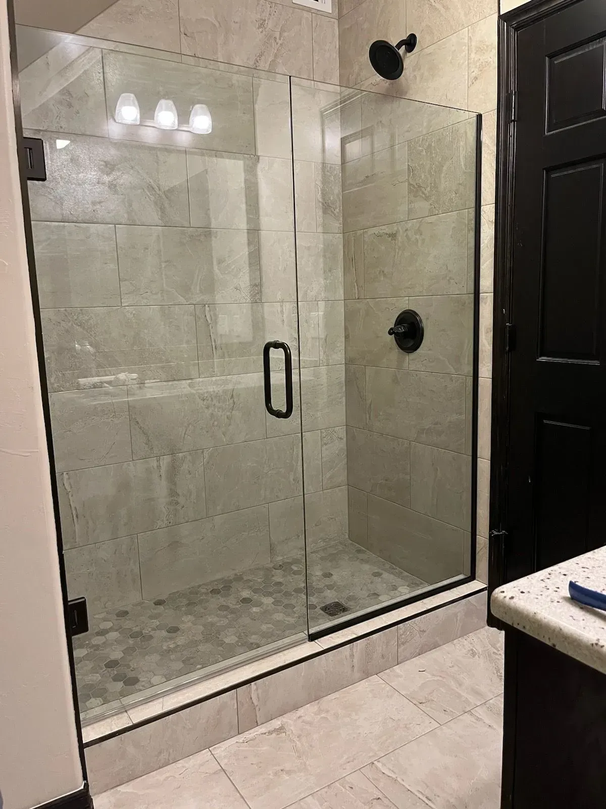 Modern bathroom with glass-enclosed tiled shower, black fixtures, and beige floor tiles